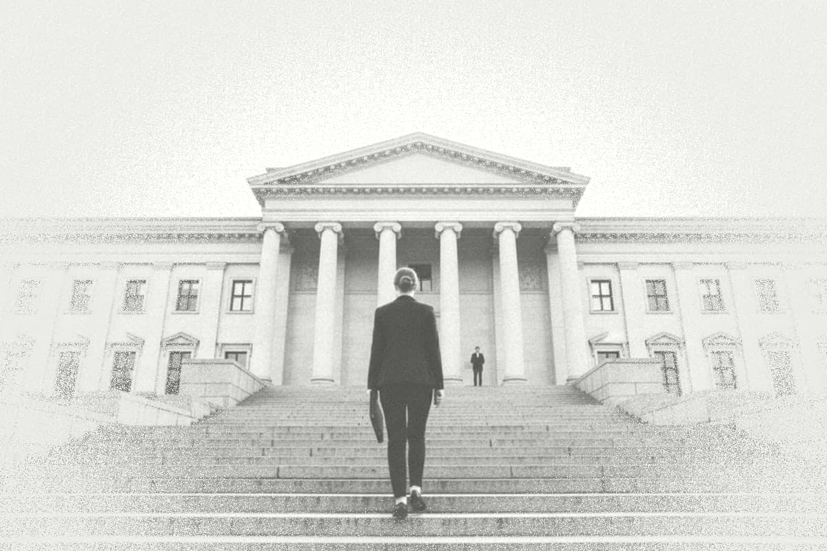A young woman with a folder walks up wide steps towards the colonnade of a parliament building.